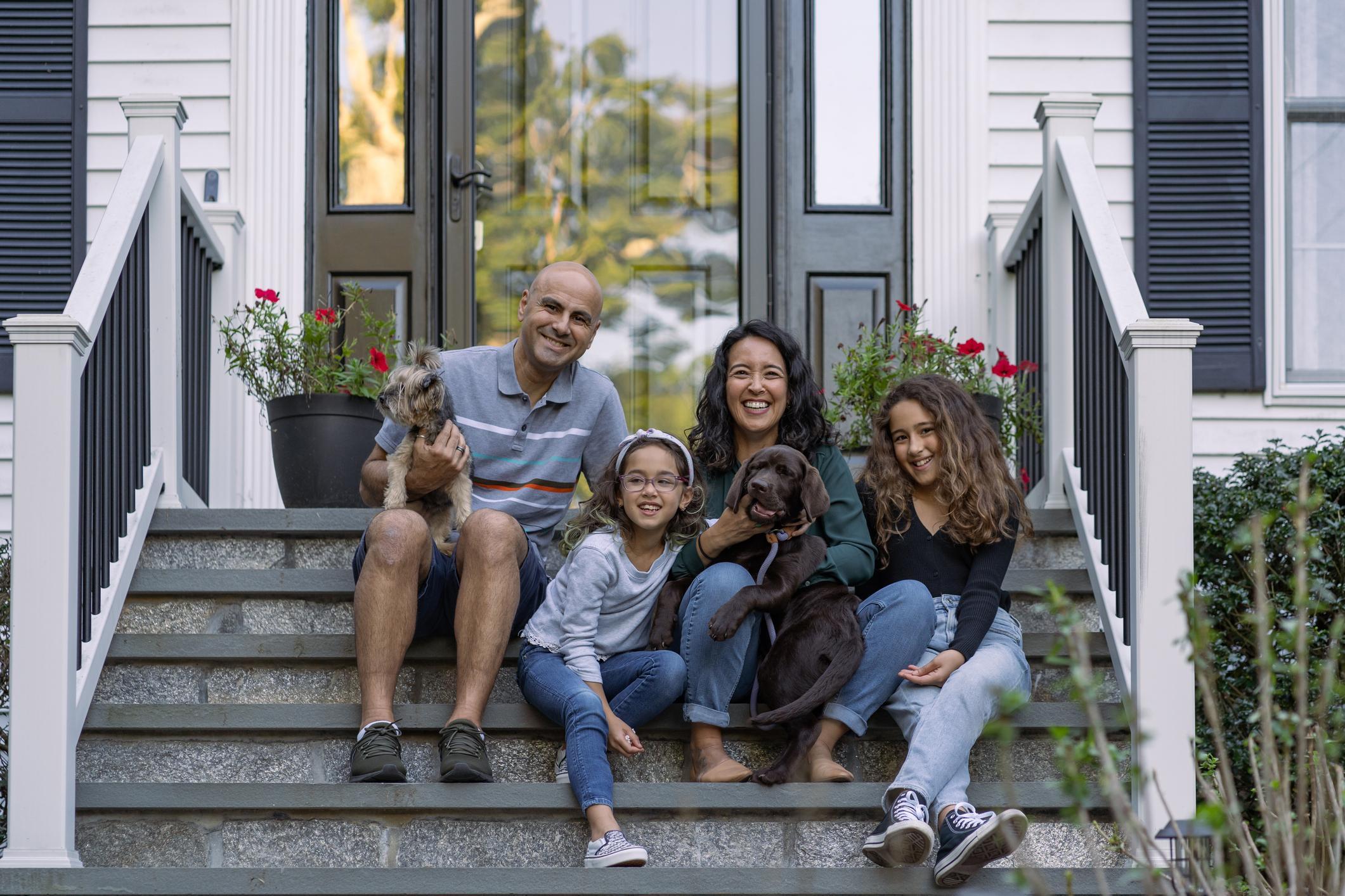 A family sitting on the steps of their house with their two dogs.