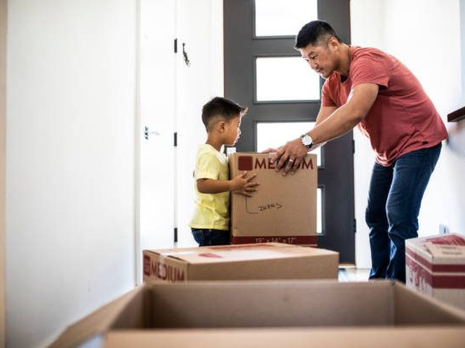 Father hands moving box to son in hallway