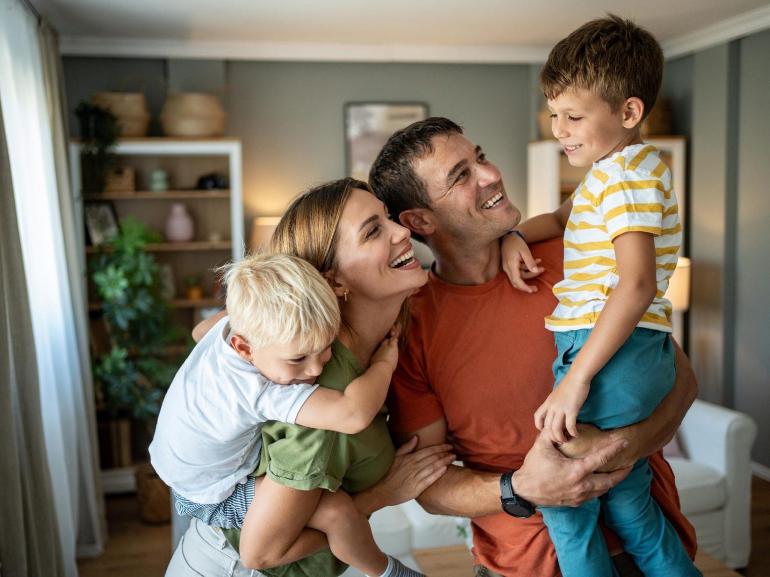 Cheerful parents joyfully carrying their two sons on their backs, creating playful moments and laughter together in the cozy living room.