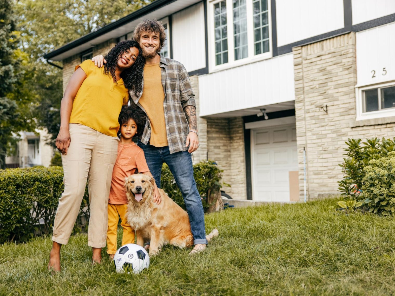 Multi-ethnic family and their dog in front of their house.