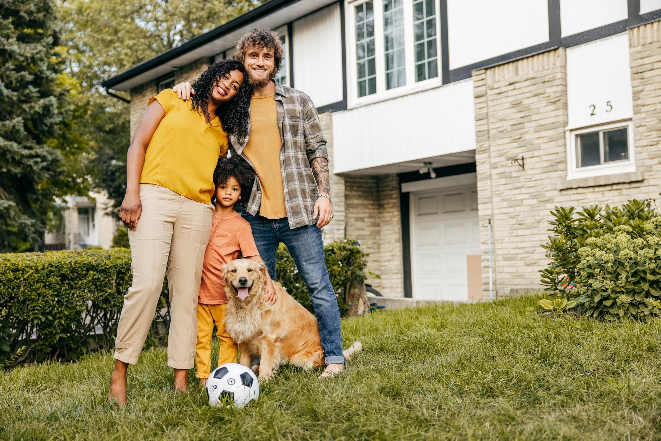 Multi-ethnic family and their dog in front of their house.